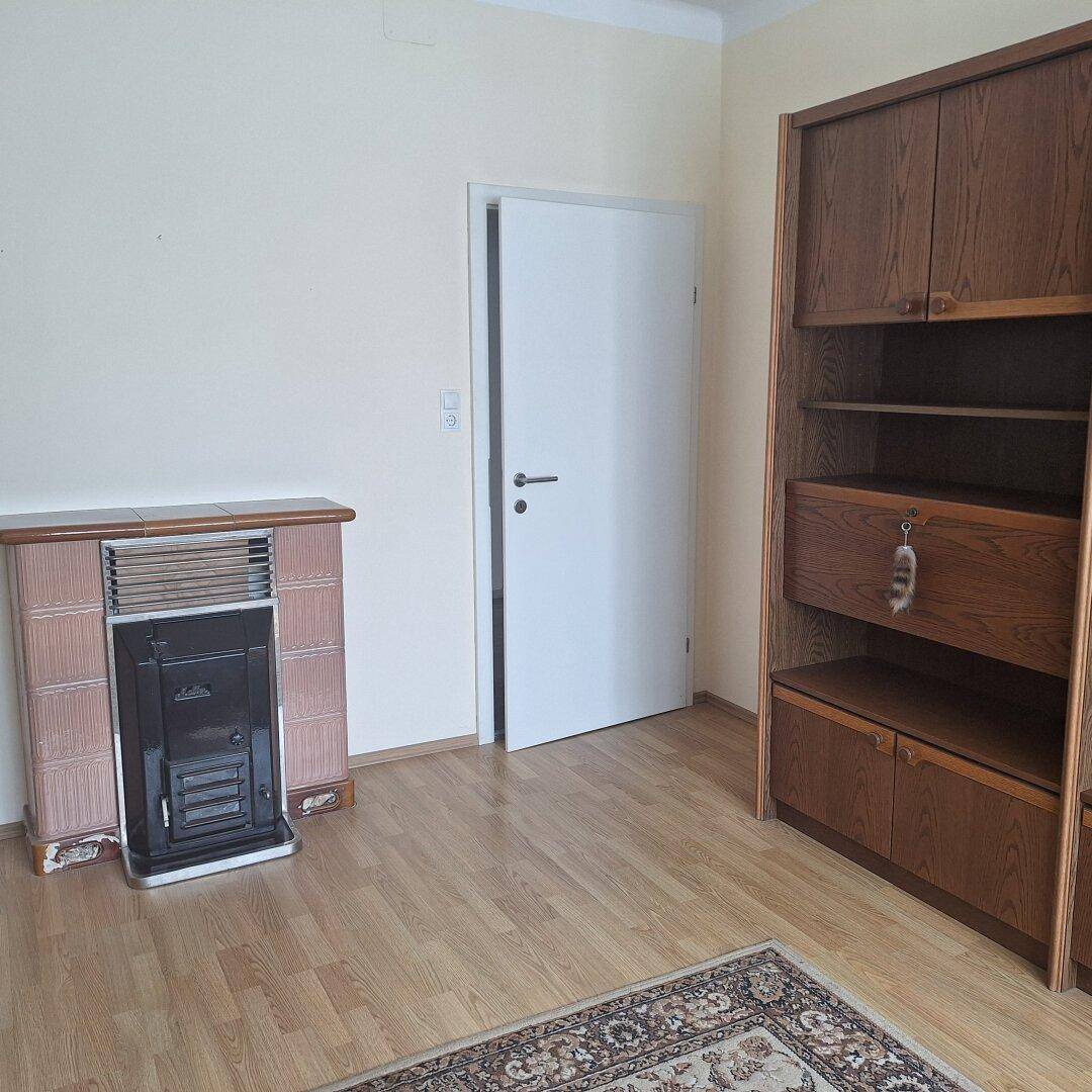 Zimmer mit traditionellem Kachelofen, Holzregal und Laminatboden.