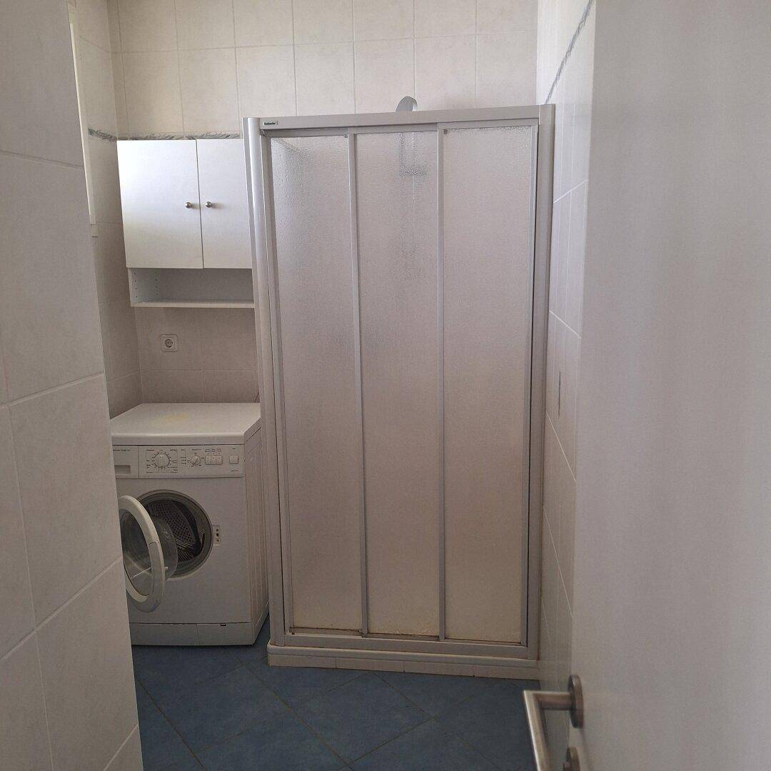 Badezimmer mit Duschkabine, Waschmaschine und blauen Bodenfliesen.
