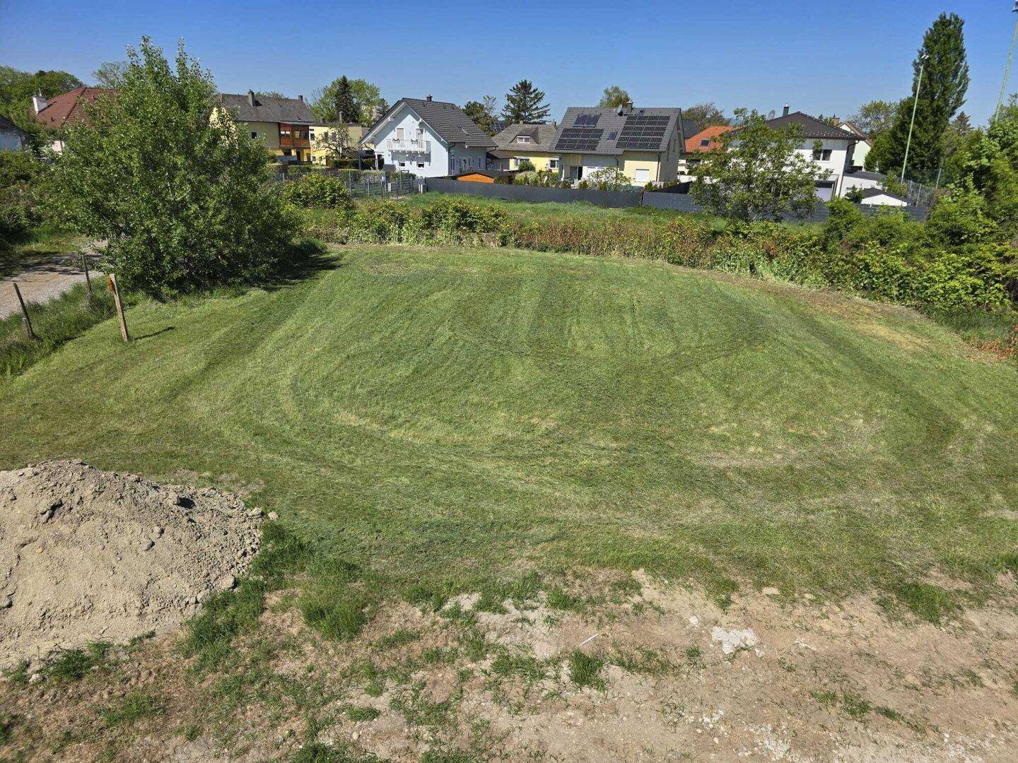 Erhöhte Perspektive auf eine grüne Rasenfläche mit umliegenden Wohnhäusern und Bäumen im Hintergrund.