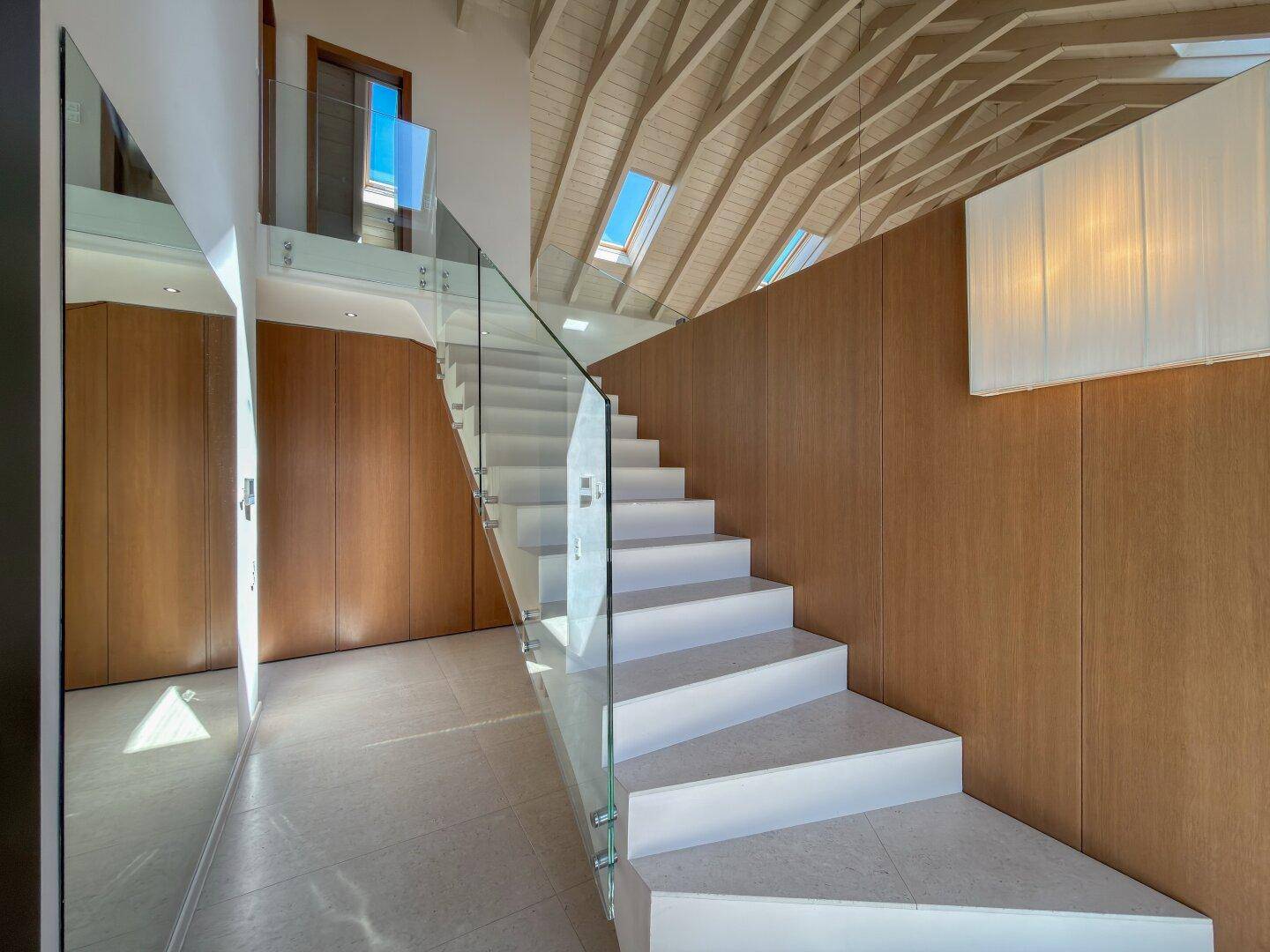 Moderne Treppe mit Glasgeländer und Holzverkleidung, die zum Dachgeschoss führt.