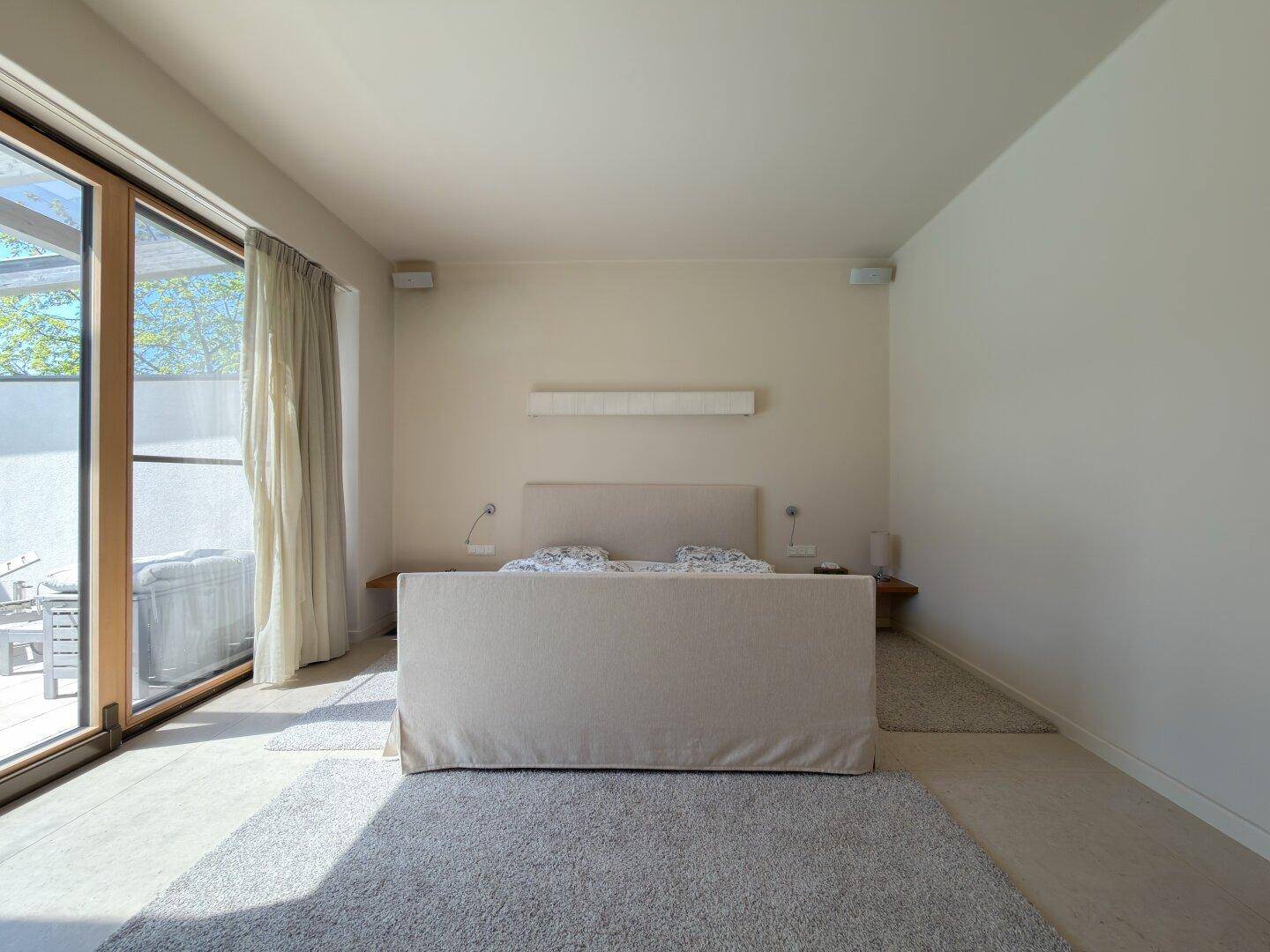 Helles Schlafzimmer mit großem Bett, Teppichboden und Zugang zu einer Außenterrasse.
