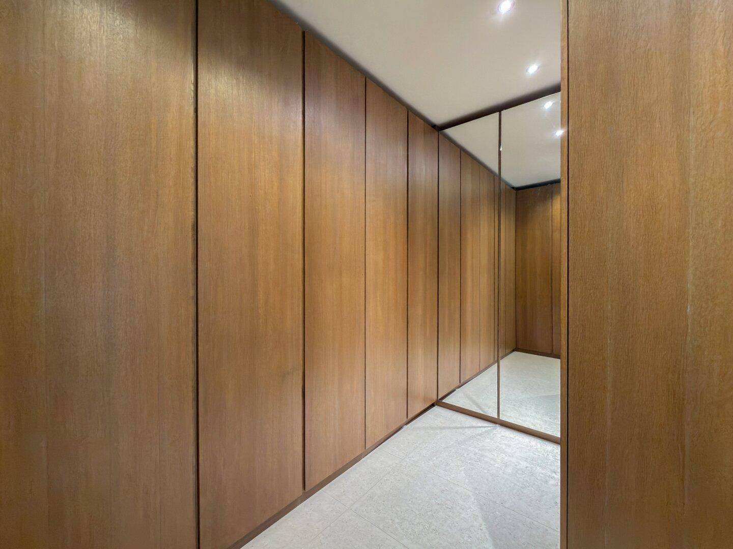 Langer begehbarer Kleiderschrank mit Holzverkleidung und Spiegeltüren für viel Stauraum.