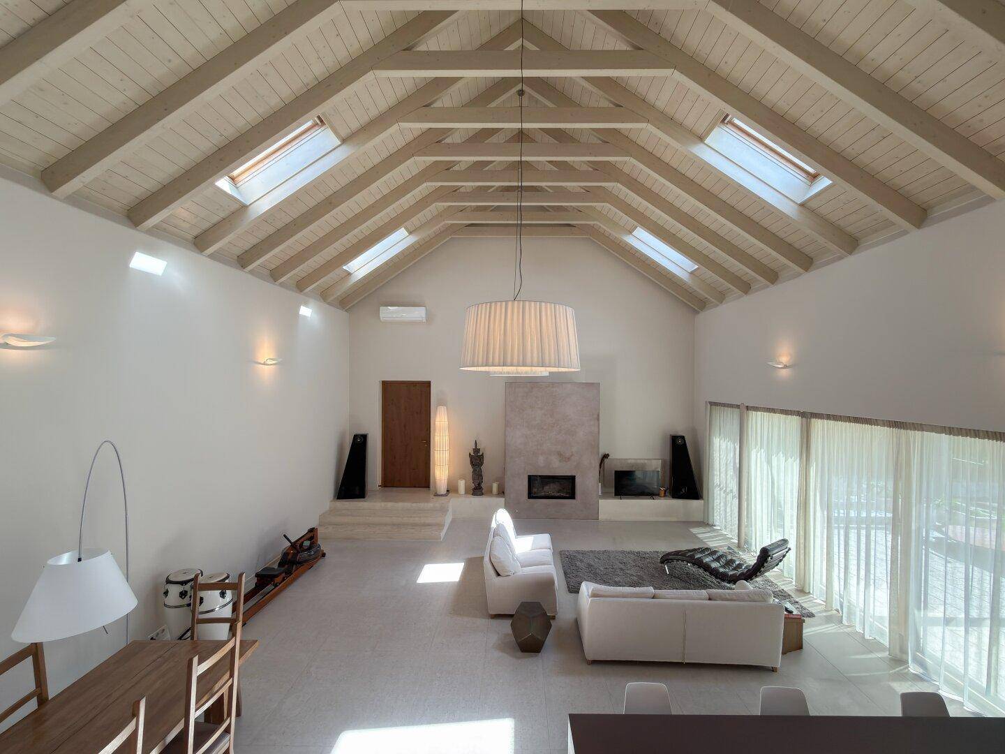Großzügiges Wohnzimmer mit hohen Holzdecken, Kamin und großen Fenstern für viel Licht.
