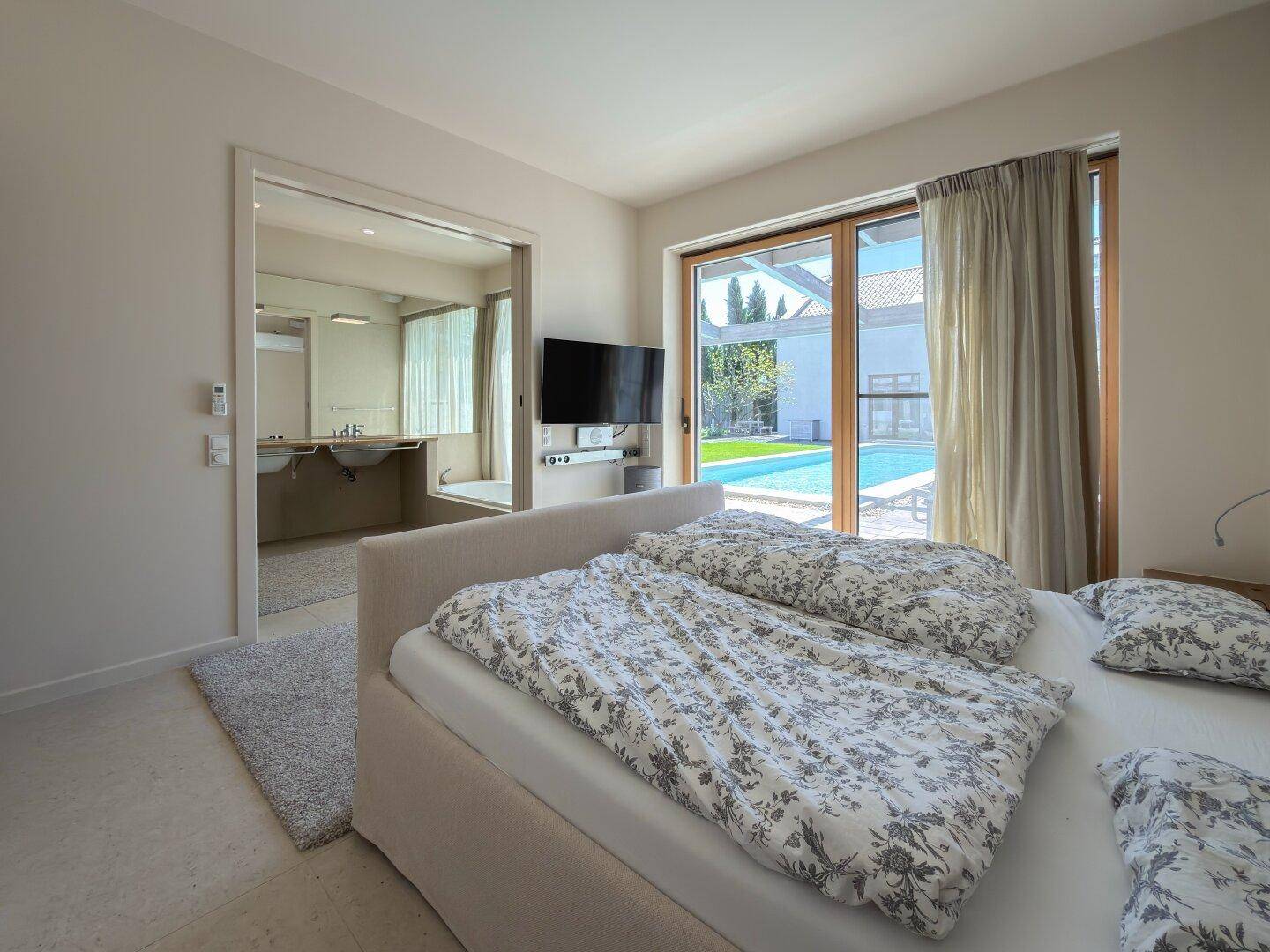 Schlafzimmer mit Blick auf den Pool, großem Bett und offenem Zugang zum Badezimmer.