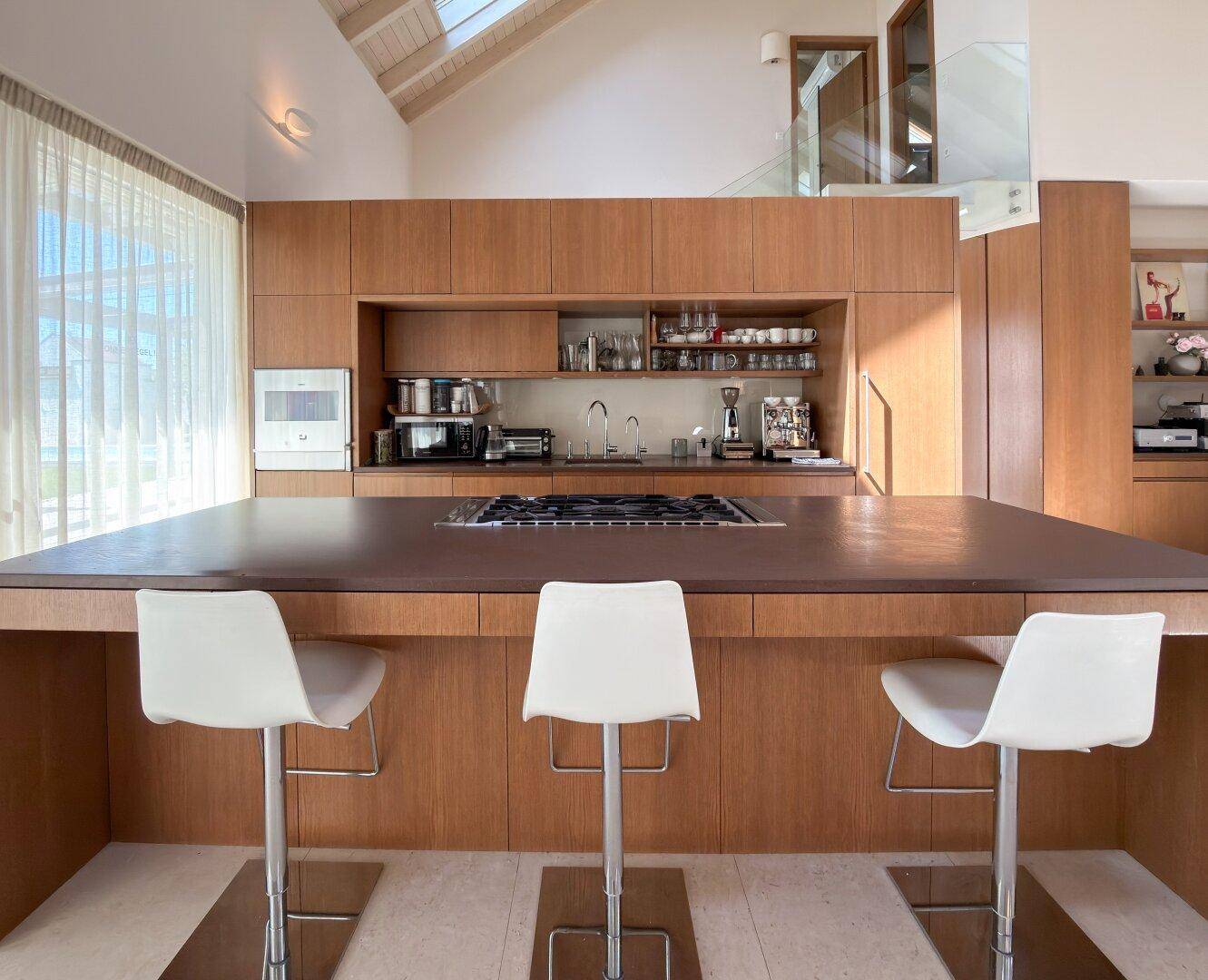 Detailansicht einer modernen Holzküche mit Kochinsel, integrierten Geräten und Barhockern.