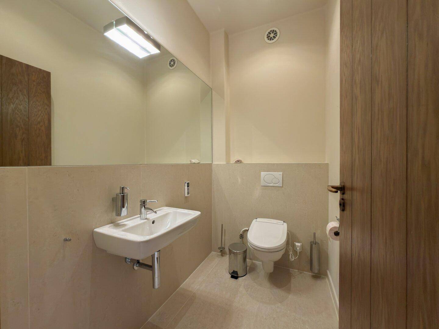Modernes Gäste-WC mit wandhängender Toilette, Waschbecken und großem Spiegel.