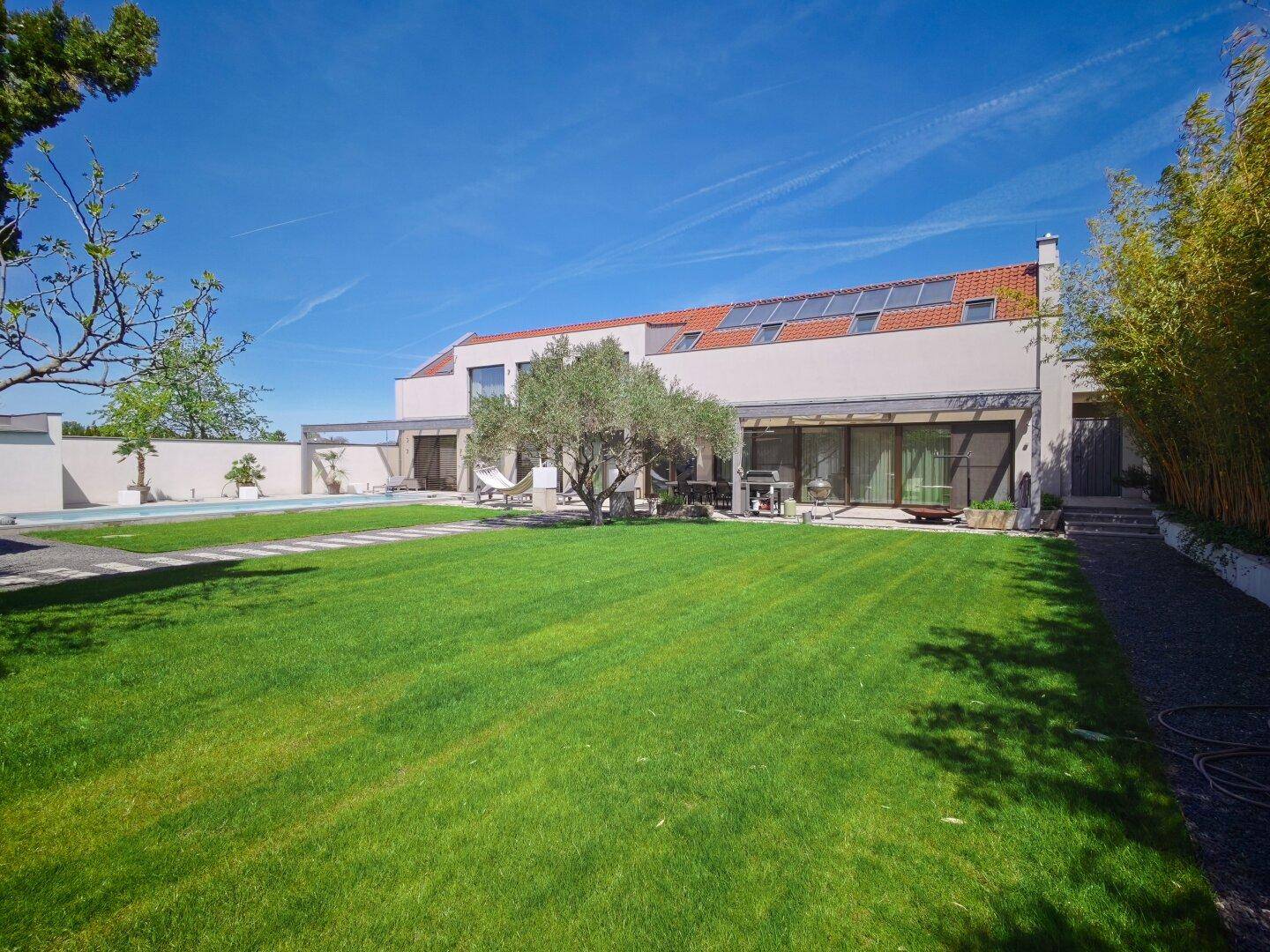 Großer gepflegter Garten mit Rasenfläche, Swimmingpool und moderner Villa mit Solaranlage.