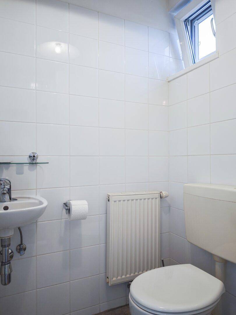 Kleines Gäste-WC mit Fenster, Waschbecken und wandmontierter Toilette.