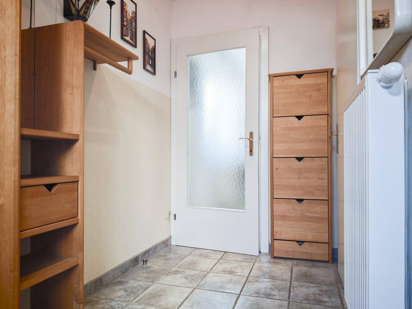 Flur mit Fliesenboden, Holzschuhschrank und einer Tür mit Milchglas.