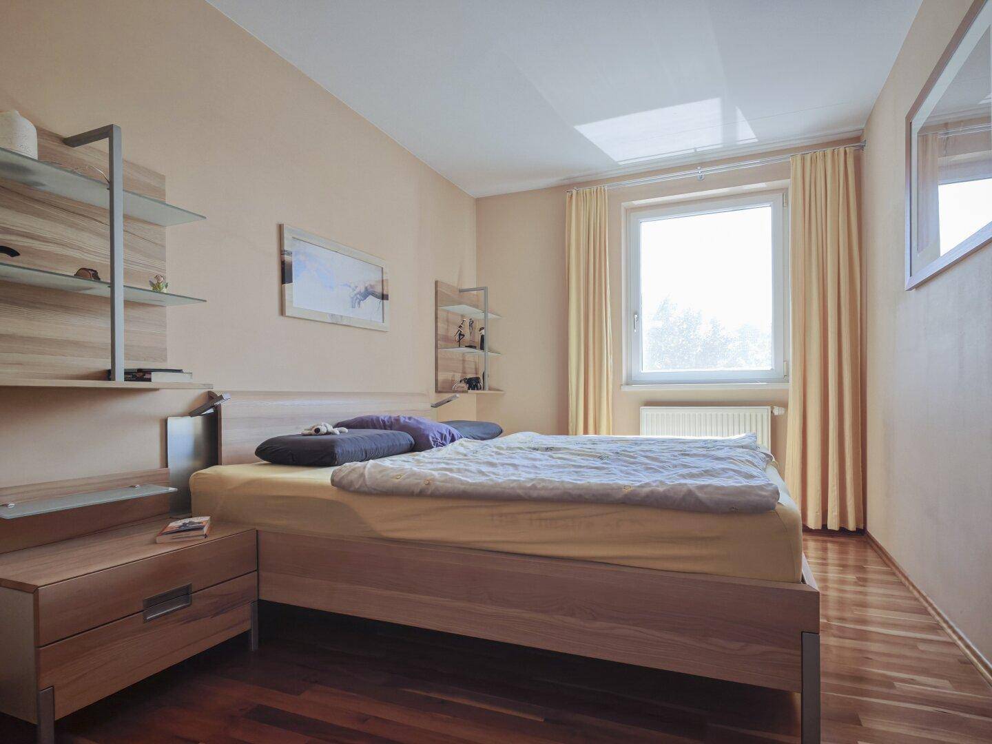 Gemütliches Schlafzimmer mit Holzbett, Parkettboden und großem Fenster für viel Licht.
