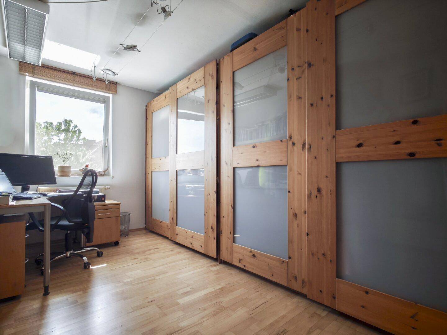 Arbeitszimmer mit großem Fenster, Schreibtisch und integrierten Holzschränken für Stauraum.