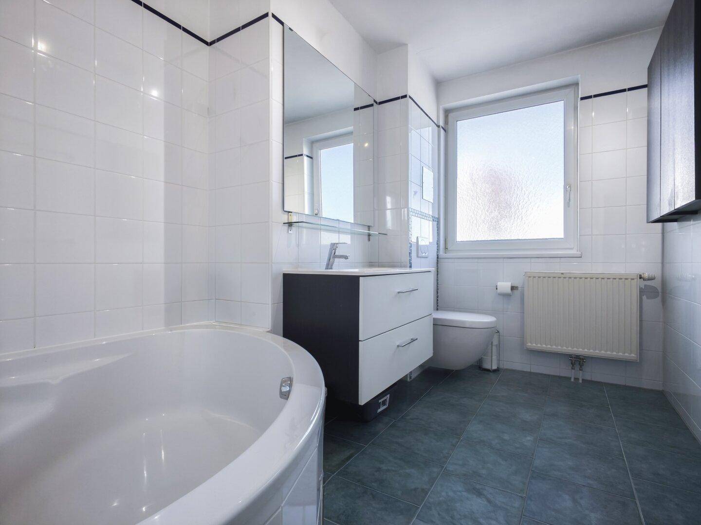 Helles Badezimmer mit Eckbadewanne, WC, Einzelwaschbecken und Fenster für Belüftung.