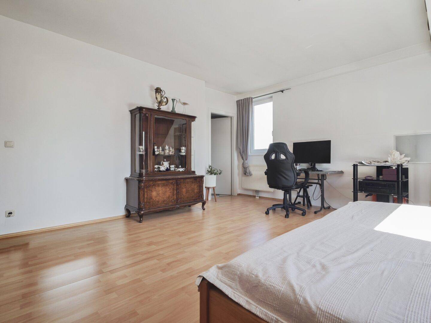 Geräumiges Schlafzimmer mit hellem Laminatboden und klassischer Vitrine, vielseitig nutzbar.