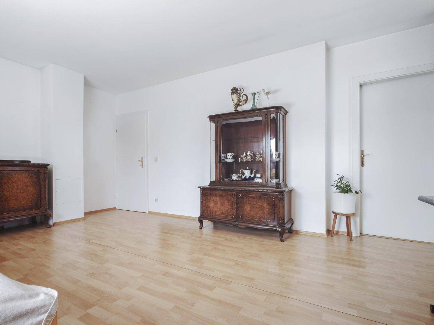 Geräumiges Wohnzimmer mit hellem Laminatboden und klassischer Vitrine, bereit zur individuellen Gestaltung.