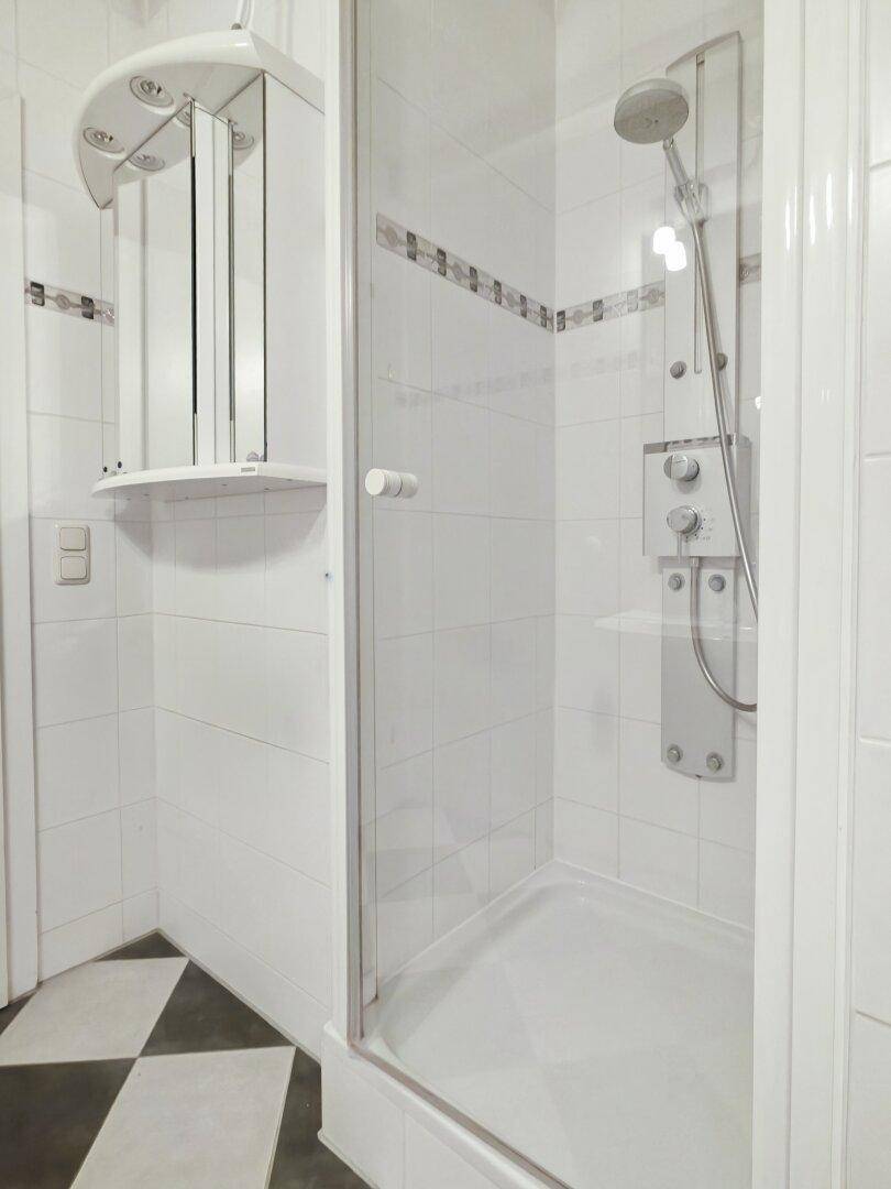 Duschbereich im Badezimmer mit Glasabtrennung und weiß gefliesten Wänden.