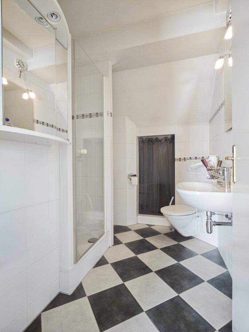 Modernes Badezimmer mit schwarz-weißem Schachbrettmuster-Fliesenboden und Duschkabine.
