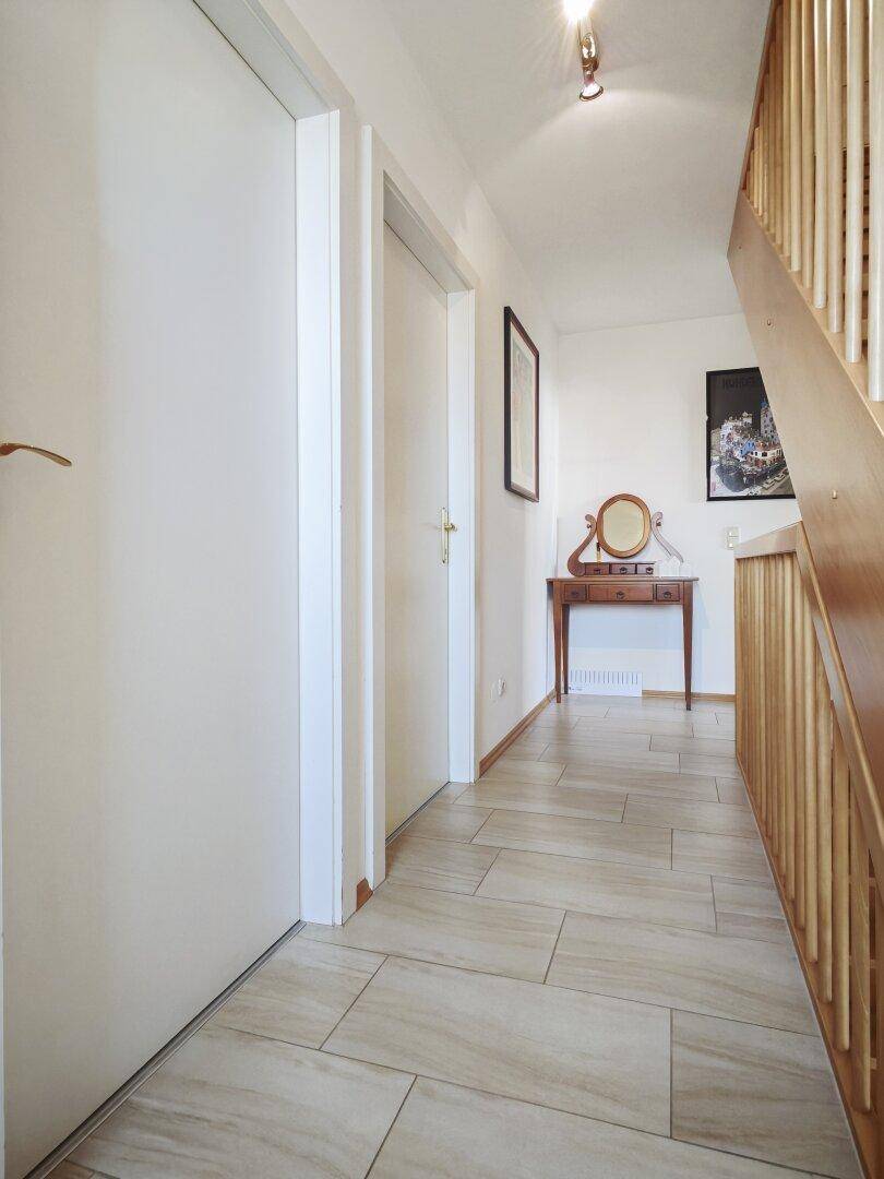 Heller Flur mit Fliesenboden, Holztreppe und klassischer Konsole mit Spiegel.