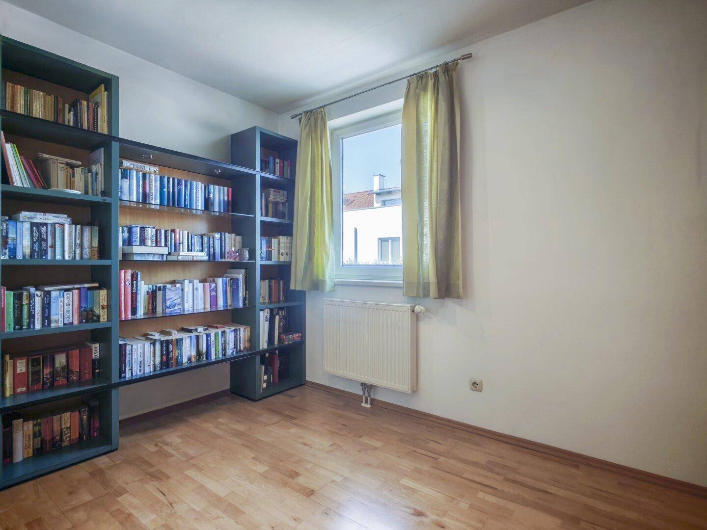 Ruhiges Arbeitszimmer mit großem Bücherregal, Fenster und hellem Parkettboden.
