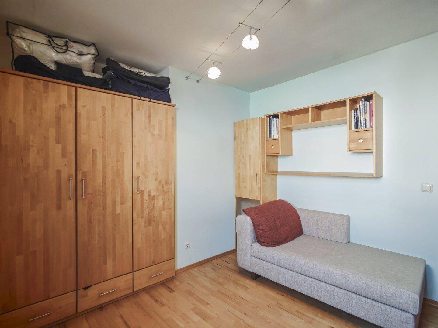Helles Zimmer mit Holzboden, großem Kleiderschrank und einer gemütlichen Liege.