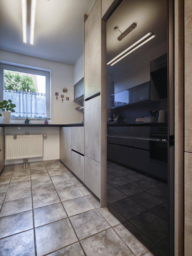Helle Küche mit modernen grauen Fronten, Fliesenboden und integriertem Kühlschrank.