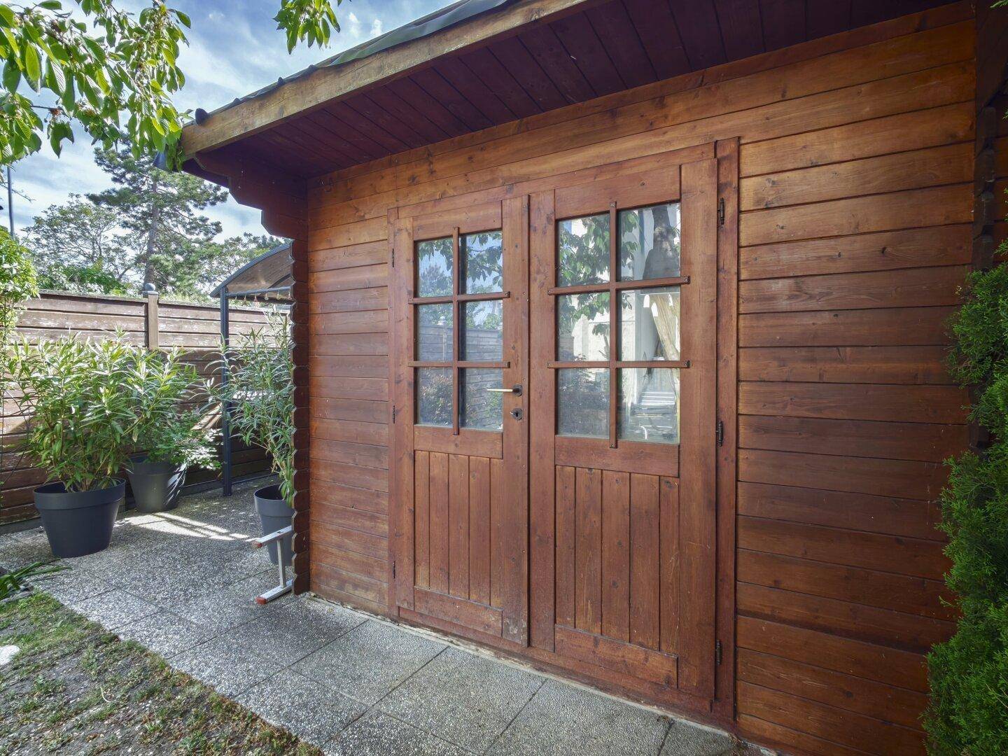 Rustikales Holzgartenhaus mit Doppeltüren und Fenstern im Grünen.