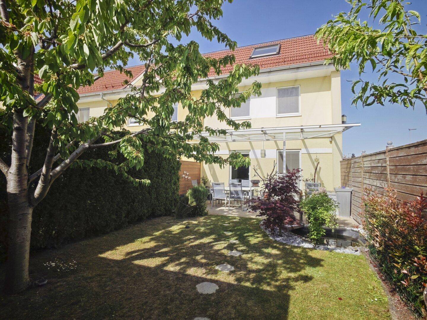 Sonniger Gartenbereich mit Terrasse, Rasen und Hecke, ideal für Entspannung im Freien.