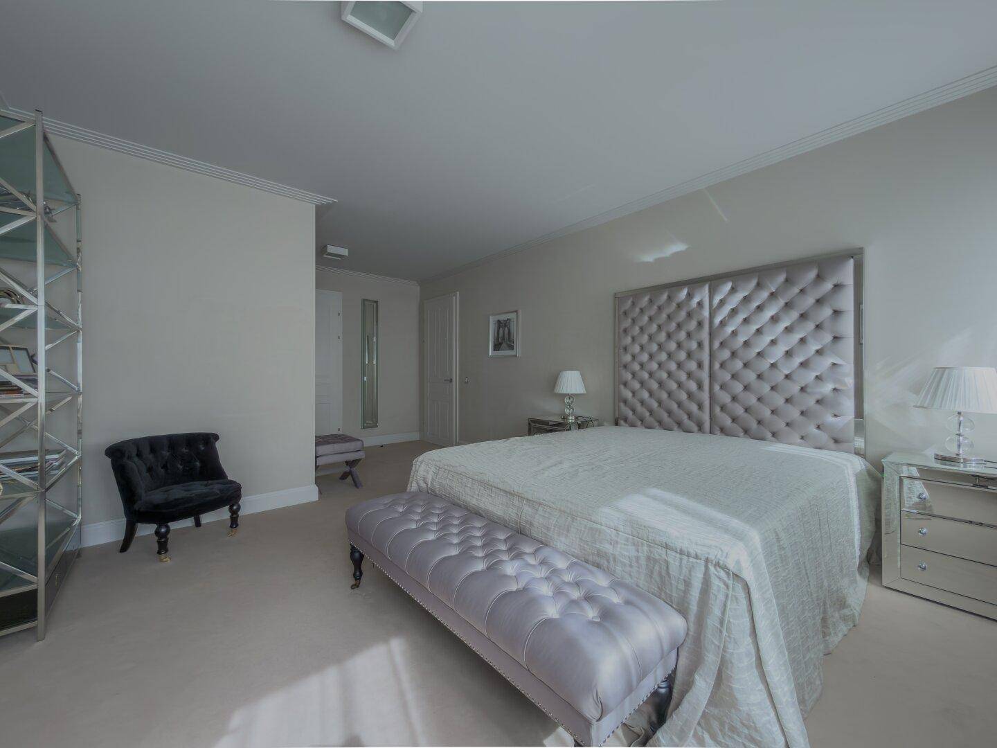 Helles Schlafzimmer mit großem gepolstertem Bett, Teppichboden und modernen Nachttischen.
