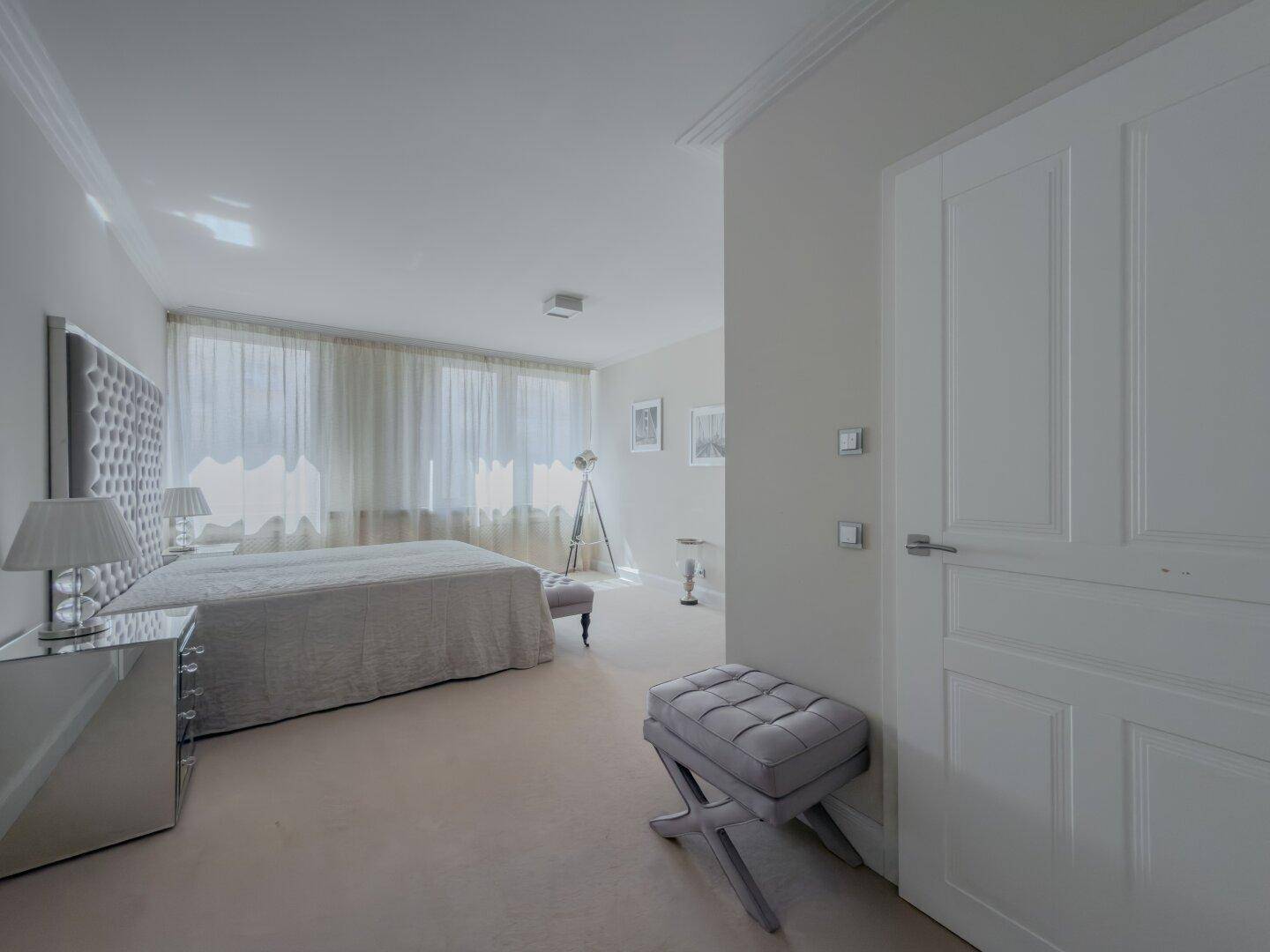 Helles Schlafzimmer mit großem Bett, Teppichboden und bodentiefen Fenstern mit Vorhängen.