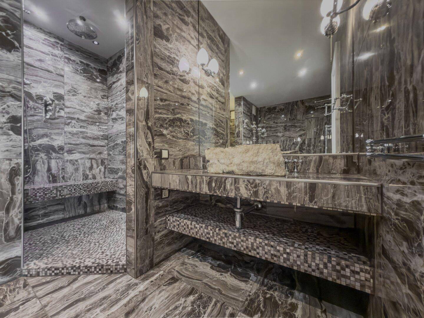 Luxuriöses Badezimmer mit dunklen Marmorfliesen, begehbarer Dusche und modernem Waschtisch.