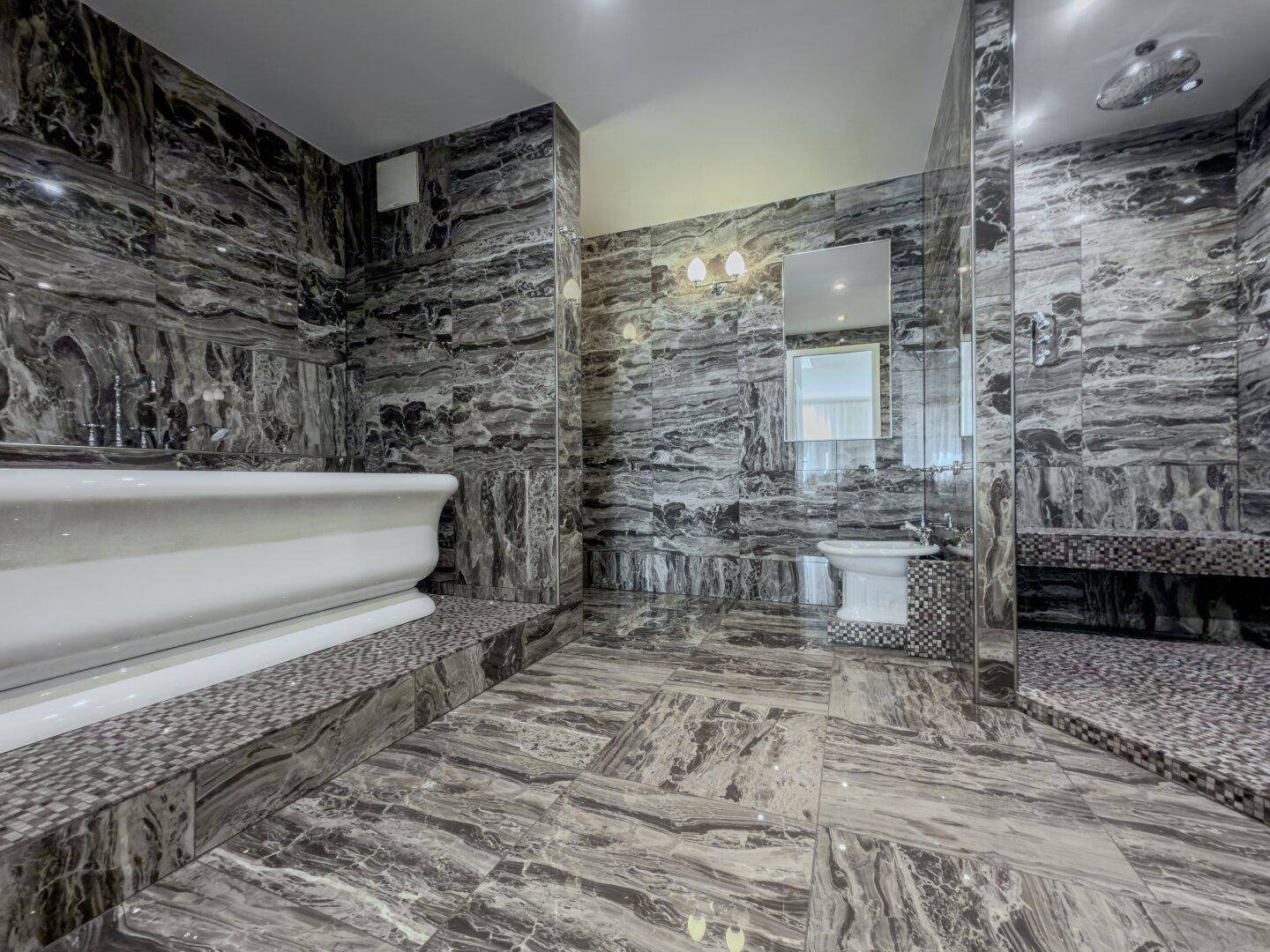 Geräumiges Luxusbadezimmer mit dunklen Marmorfliesen, freistehender Badewanne und begehbarer Dusche.