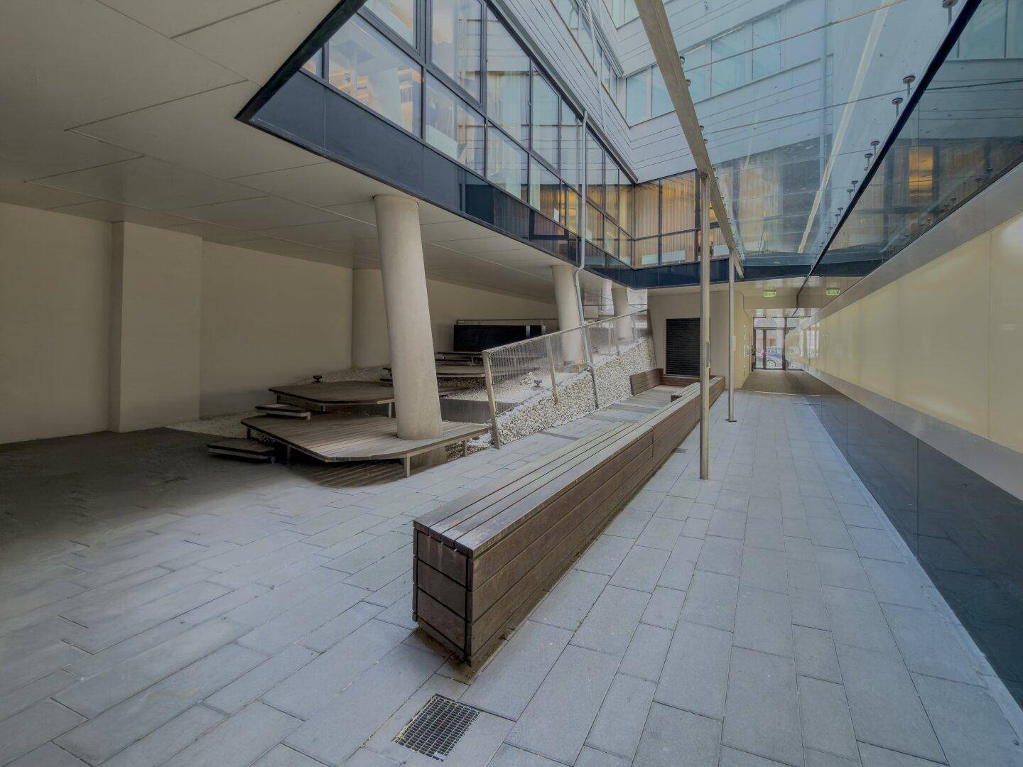 Moderner Außenbereich mit Sitzgelegenheiten und architektonischen Elementen unter einer Glasüberdachung.