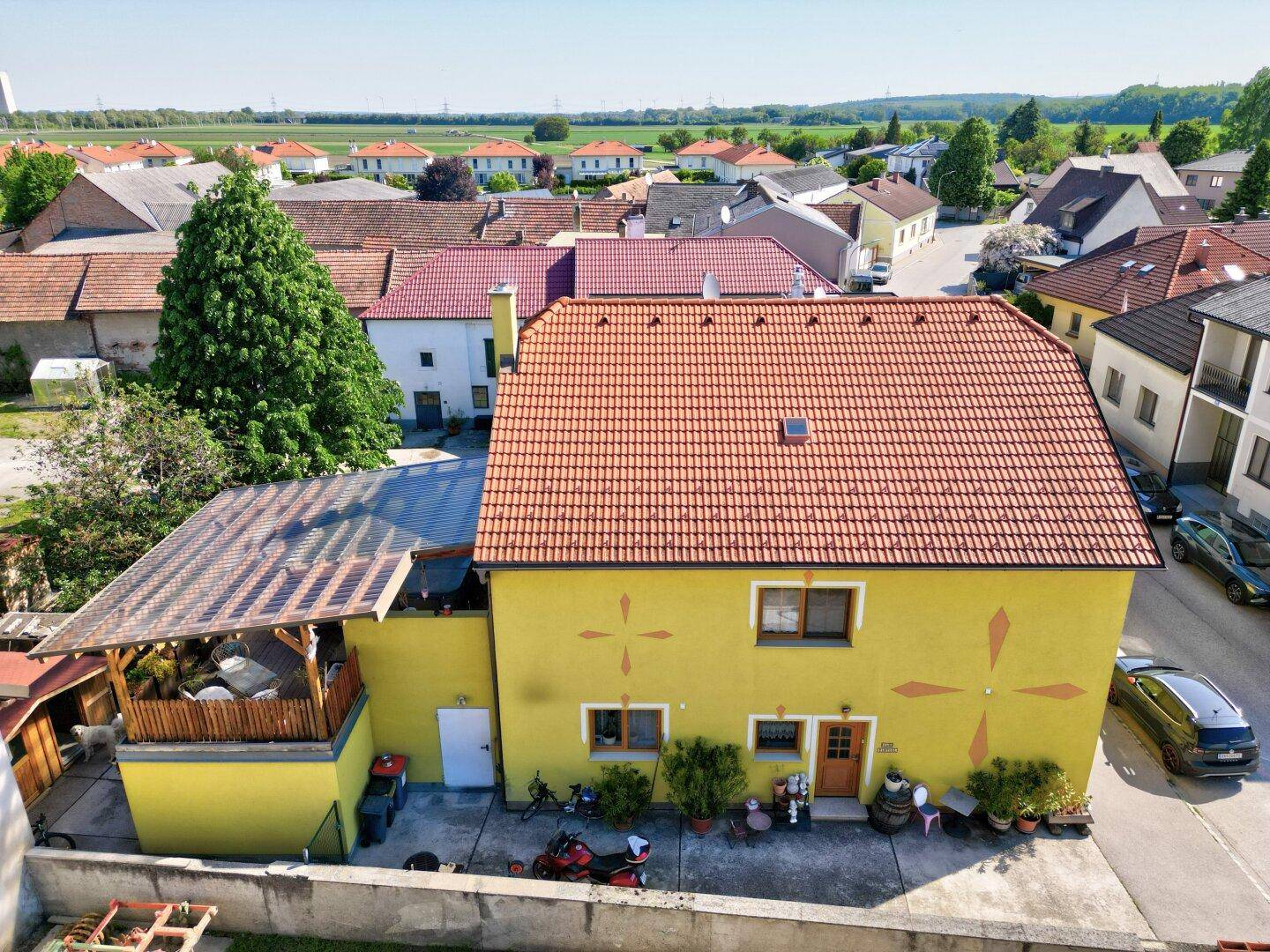 Luftaufnahme eines gelben Hauses mit rotem Ziegeldach in einer ländlichen Umgebung.