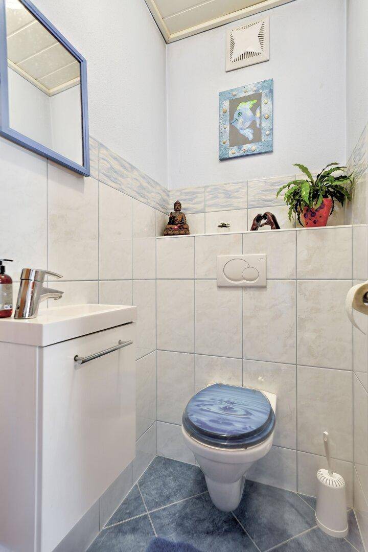 Kleines Gäste-WC mit Wand-WC, Waschbecken und blauen Akzenten.
