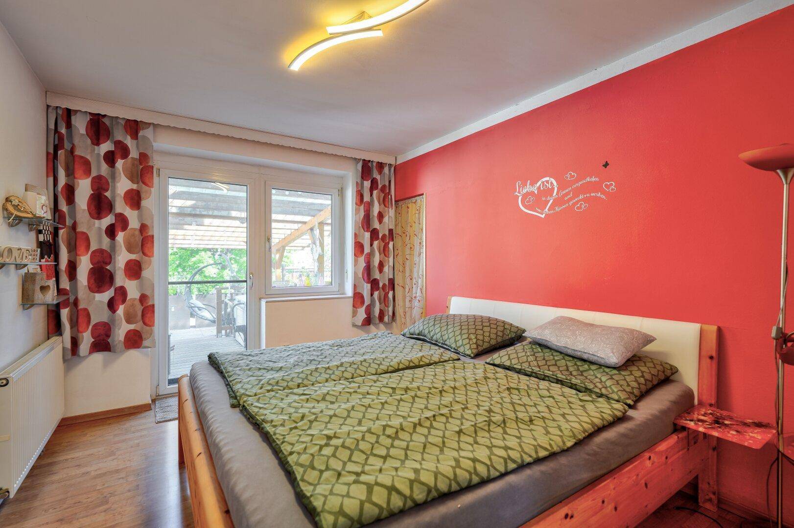 Gemütliches Schlafzimmer mit Doppelbett, roter Wand und direktem Terrassenzugang.