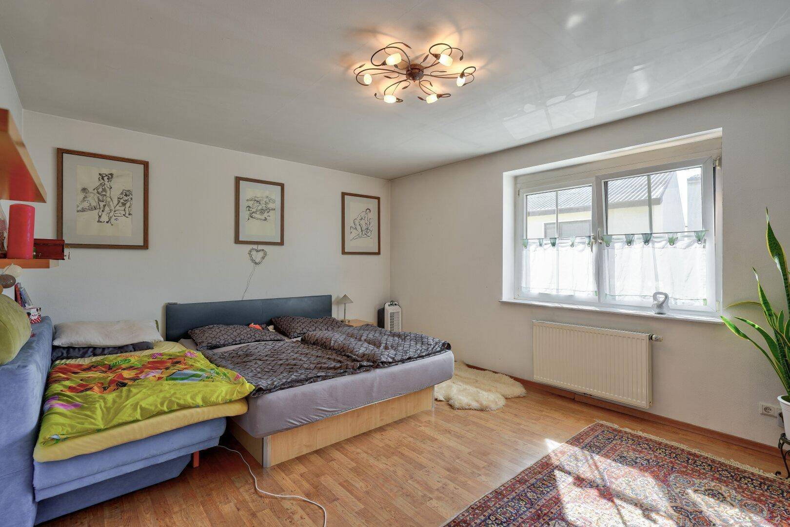 Gemütliches Schlafzimmer mit Holzboden, Doppelbett und einem Fenster mit Blick nach draußen.