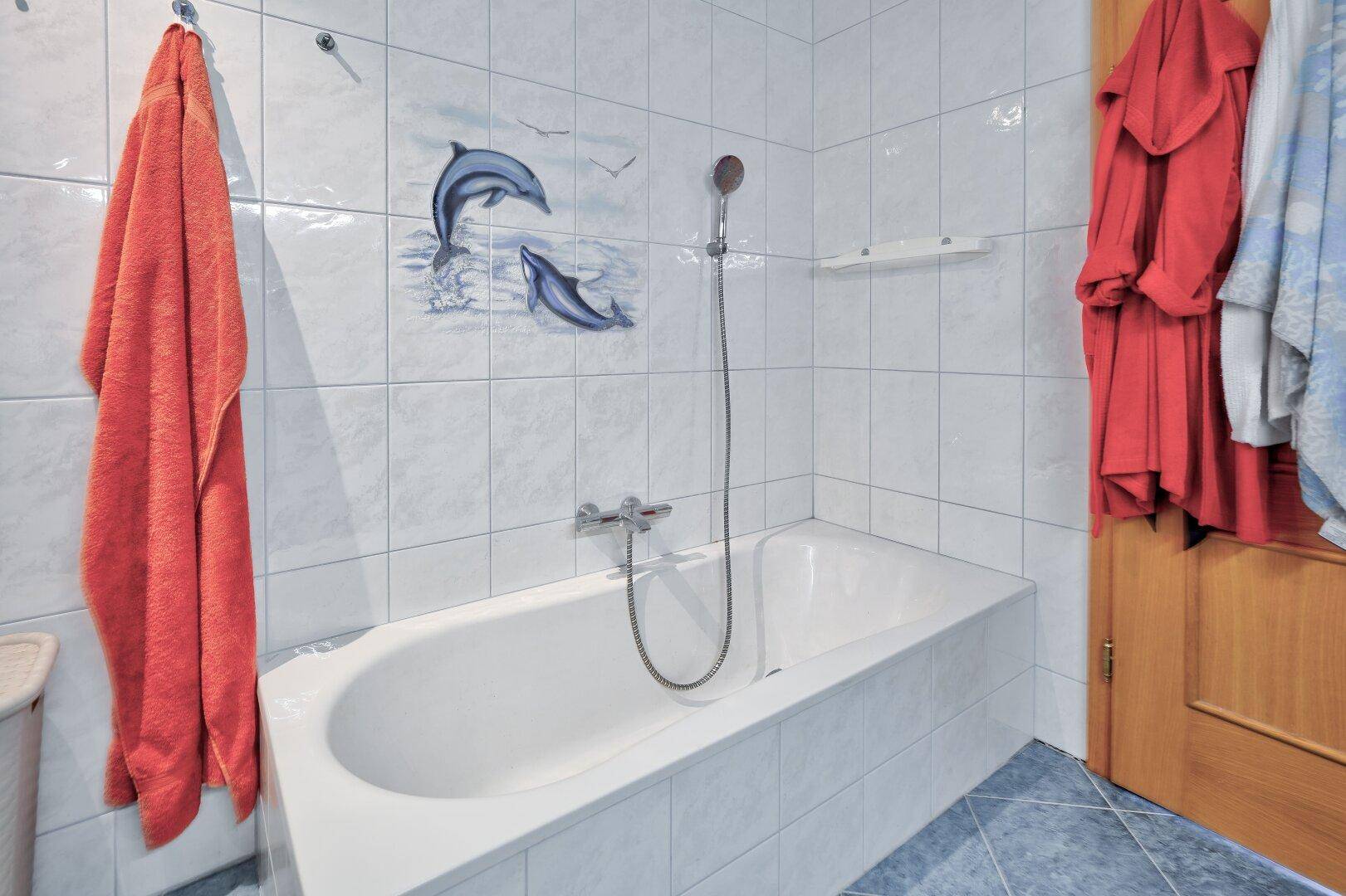 Badewanne in einem gefliesten Badezimmer mit blauen Akzenten und Duscharmatur.