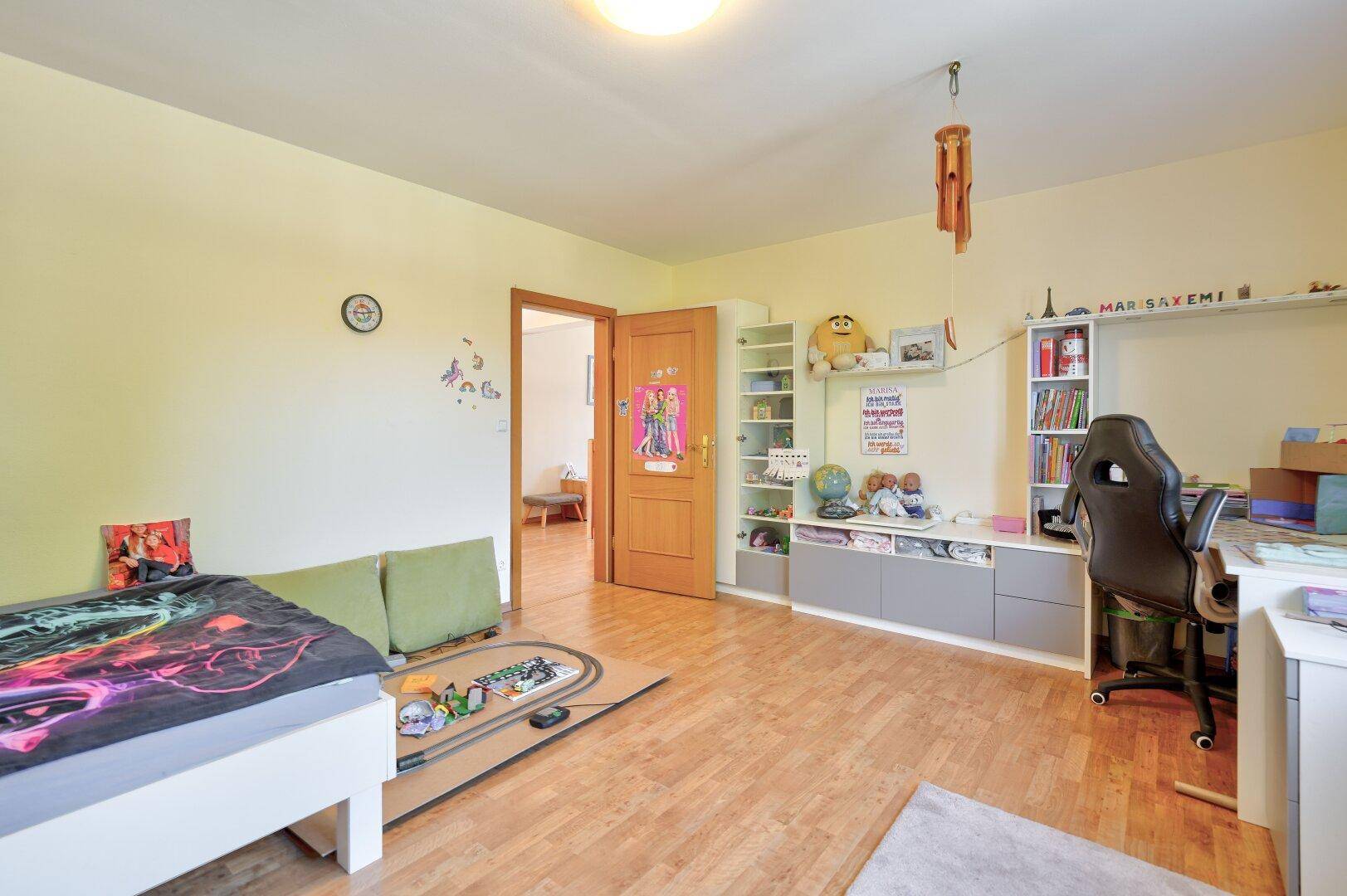 Kinderzimmer mit Holzboden, Bett und Regalen für Spielzeug und Bücher.