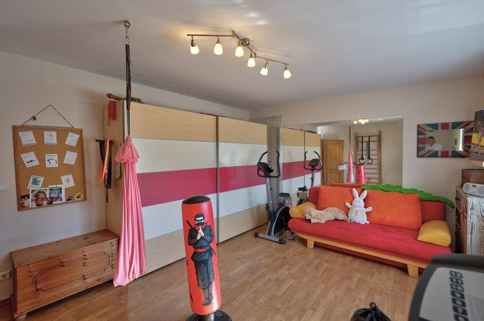 Vielseitiger Raum mit Fitnessgeräten, Sofa und Spiegelfronten für sportliche Aktivitäten.