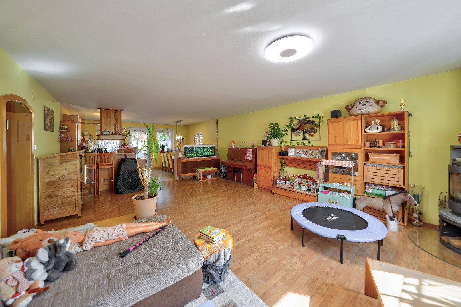Weitläufiger Wohnbereich mit Holzboden, Sofa und Blick auf die offene Küche.
