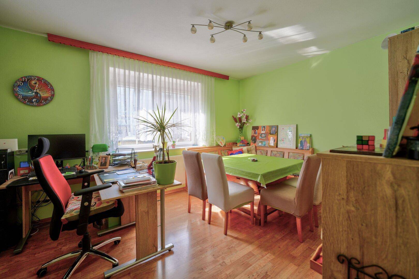 Helles Arbeitszimmer mit Schreibtisch, Esstisch und grün gestrichenen Wänden.