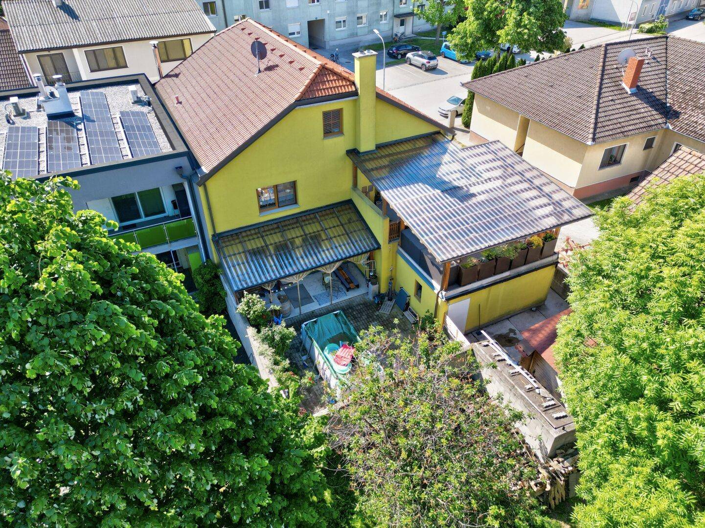 Vogelperspektive des gelben Hauses mit Garten und benachbarten Gebäuden in grüner Umgebung.