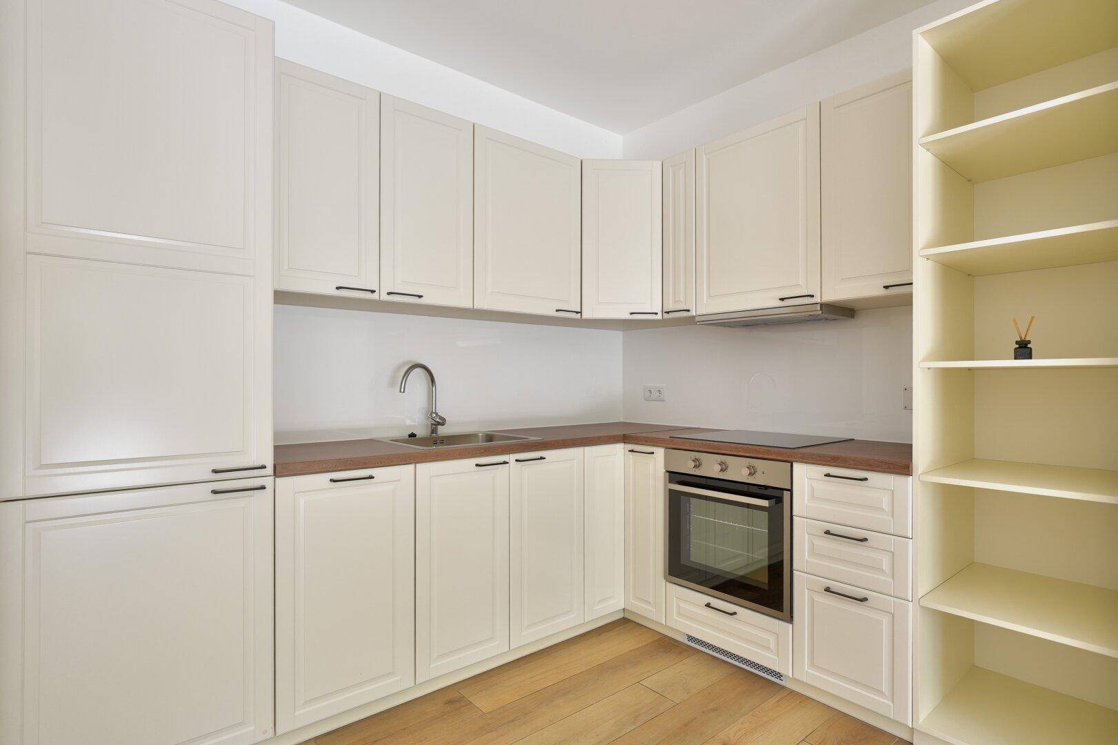 Moderne Einbauküche in hellem Cremeton mit Holz-Arbeitsplatte und integrierten Geräten.