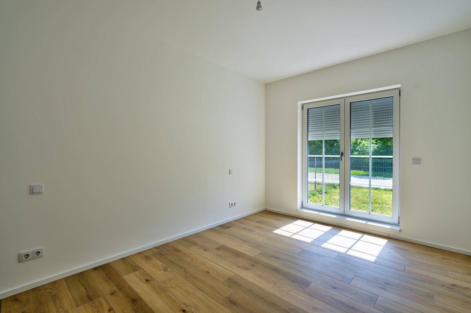 Helles Schlafzimmer mit Holzboden und großem Fenster mit Rollladen.