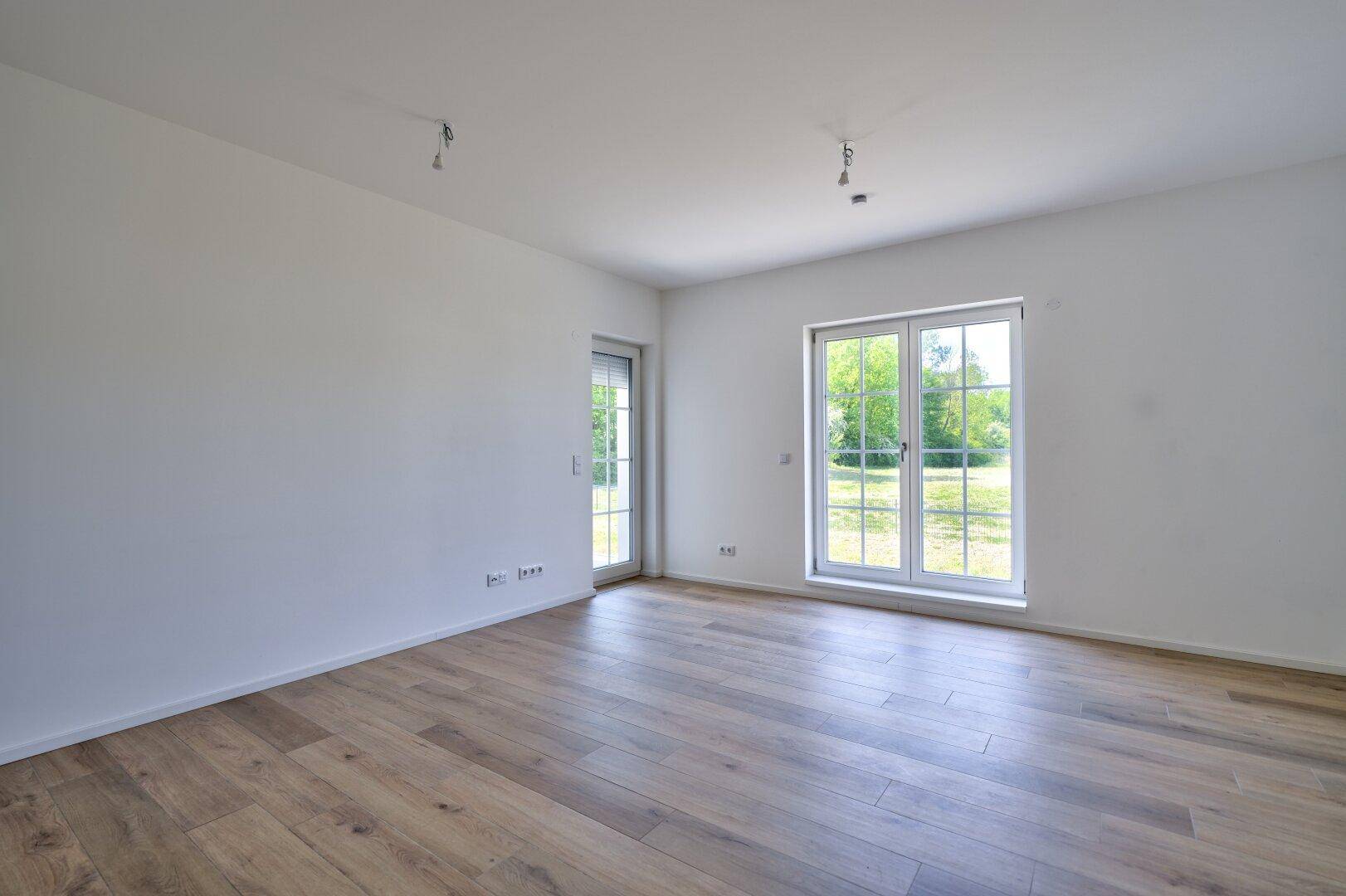 Heller, leerer Raum mit Holzboden und großen Fenstern, die viel Tageslicht hereinlassen.