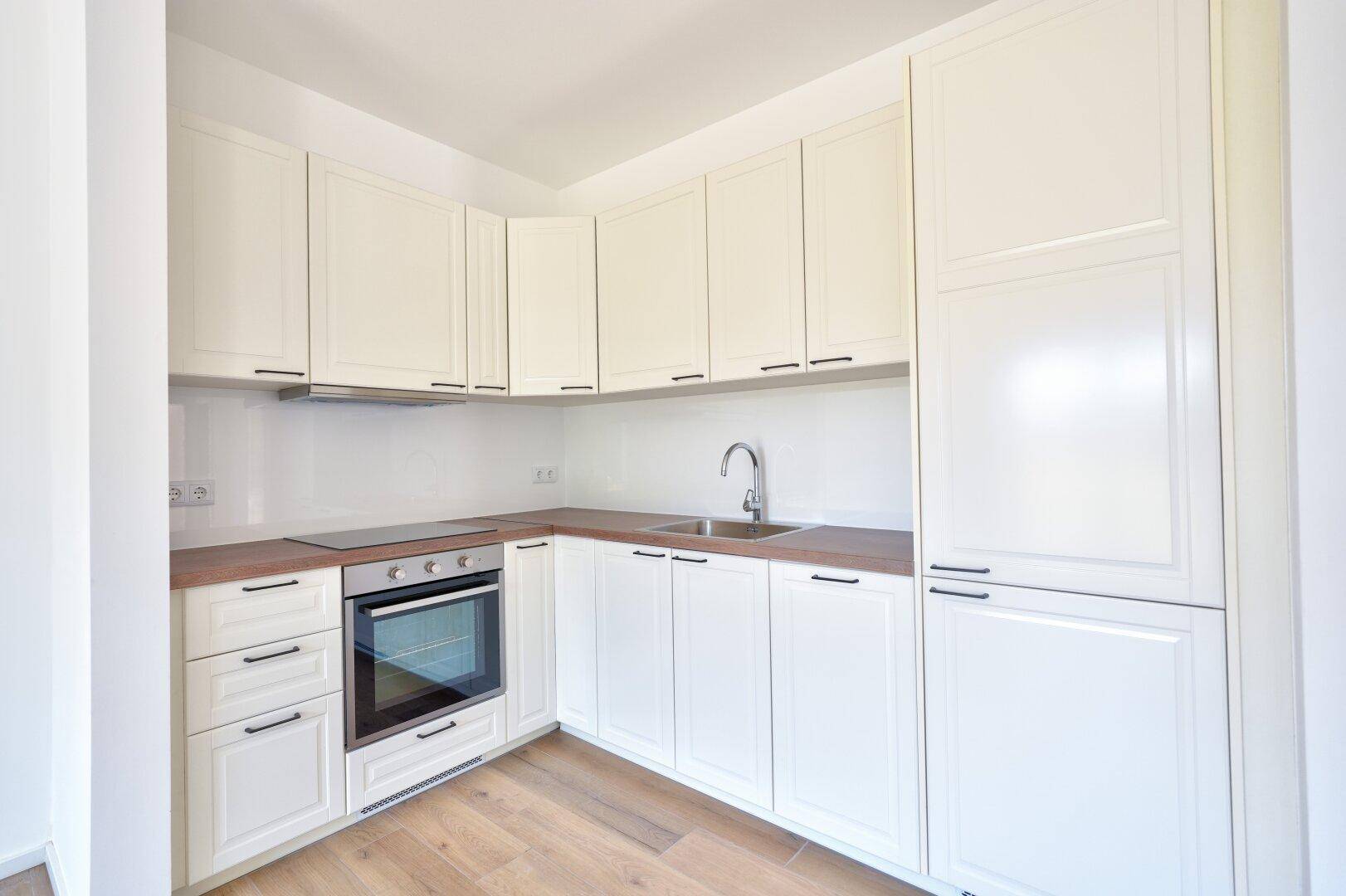 Moderne Einbauküche mit weißen Schränken, Holz-Arbeitsplatte und integrierten Geräten.