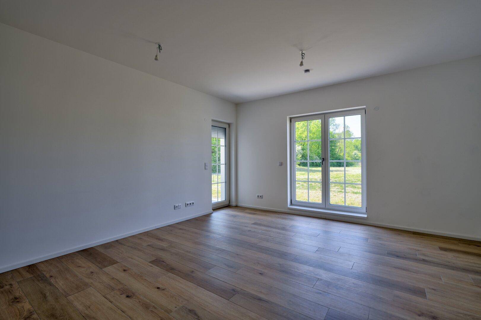 Heller, leerer Raum mit Holzboden und großen Fenstern, die viel Tageslicht hereinlassen.