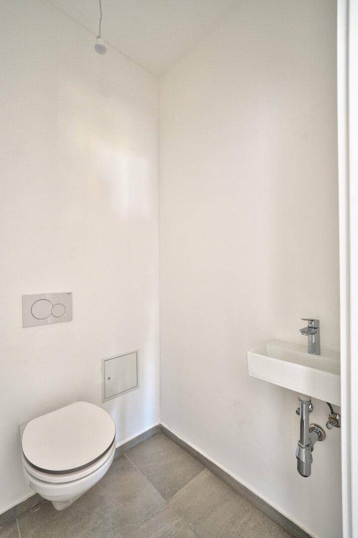 Modernes Gäste-WC mit wandhängender Toilette und kleinem Waschbecken, in hellen Farben gehalten.