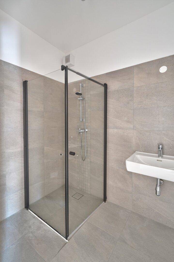 Modernes Badezimmer mit begehbarer Dusche, grauen Fliesen und einem Waschbecken.