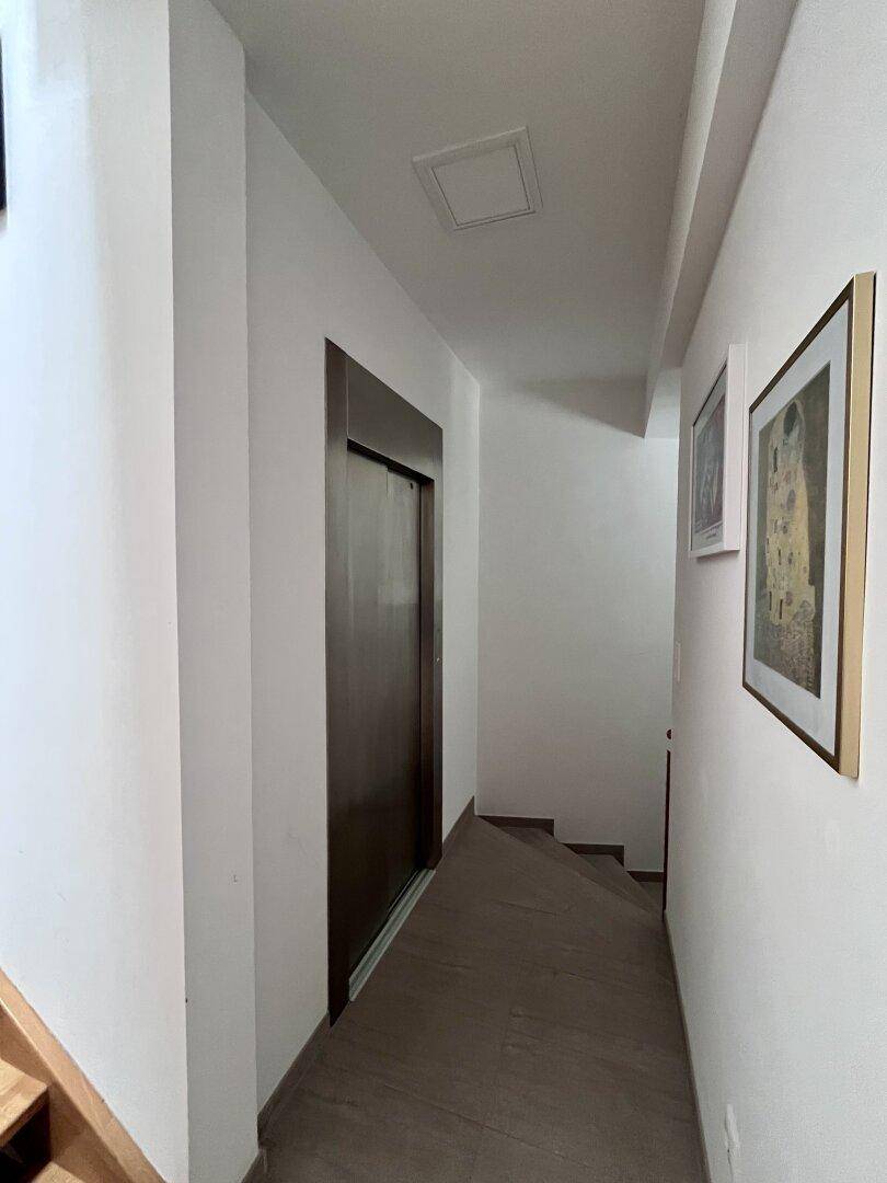 Heller Flur mit Aufzug und Kunstwerken an den Wänden.