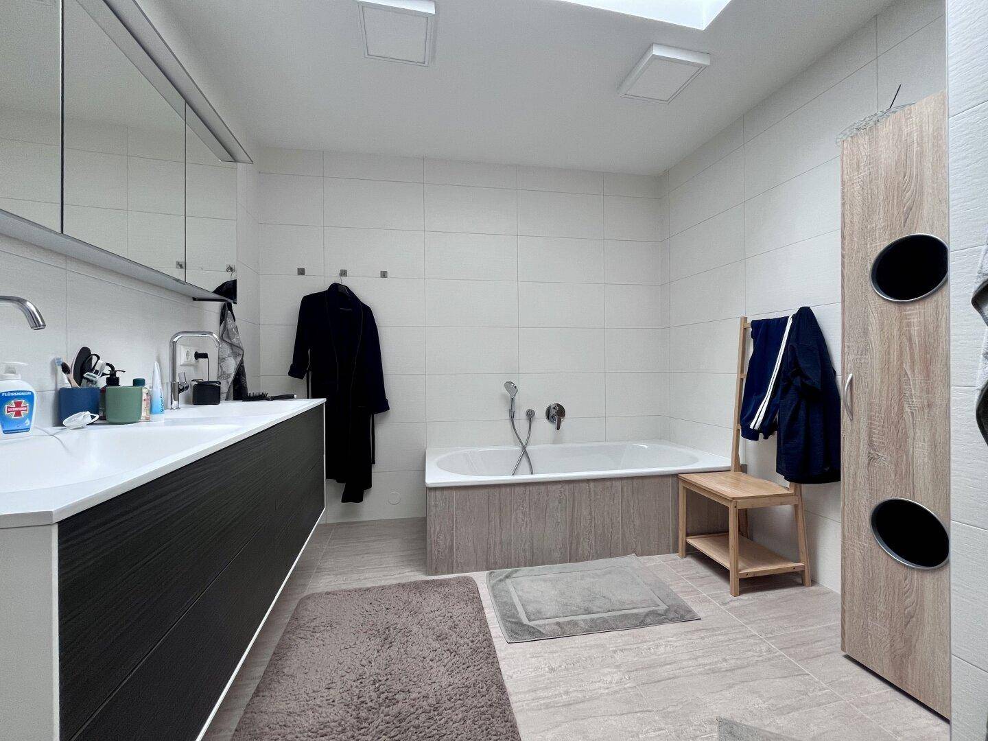 Modernes Badezimmer mit Doppelwaschbecken, Badewanne und hellen Fliesen.